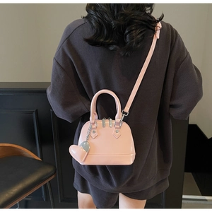 Pink shell bag with glossy finish featuring heart charm and adjustable strap detail