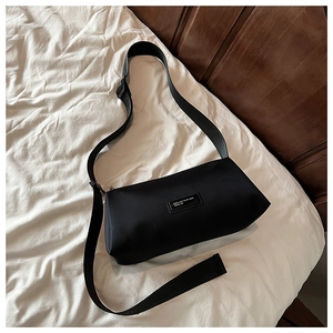 Détail d'un sac bandoulière en nylon noir avec écusson logo sur un drap blanc