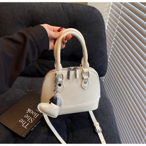 Detail of minimalist shell-shaped handbag in off-white leather with heart charm