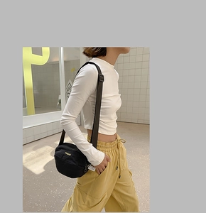 Close-up of black nylon crossbody bag with yellow logo detail worn by a model