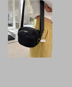 Close-up of lightweight black nylon crossbody bag featuring gold logo embroidery detail