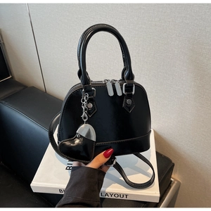 Detail of black patent leather shell bag with heart charm and detachable chain strap