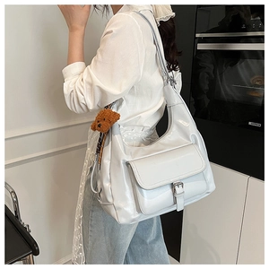 Silver crescent shoulder bag with front pocket and plush teddy bear charm in modern interior