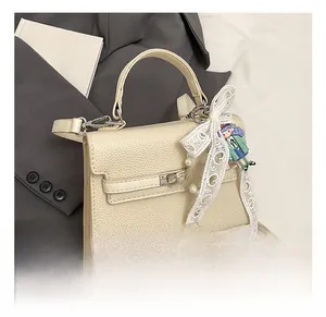 Détail du sac à main blanc cassé avec motif litchi, nœud en dentelle et chaîne perle