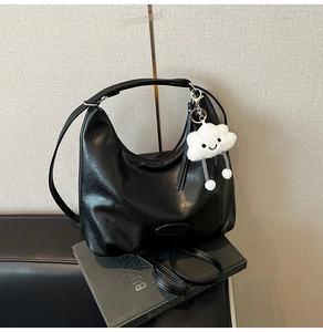 Détail d'un sac cabas en cuir noir avec breloque nuage blanc sur des livres de business