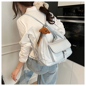 Detail shot of light grey patent leather backpack with cute teddy bear charm on model