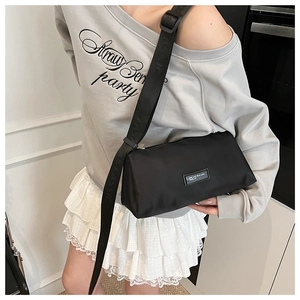 Détail du sac bandoulière en nylon noir avec large sangle texturée et écusson logo minimaliste