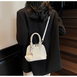 Detail view of cream shell-shaped handbag featuring a heart charm and silver hardware