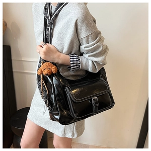 Detail view of a black glossy hobo bag with a decorative silk scarf and teddy bear charm