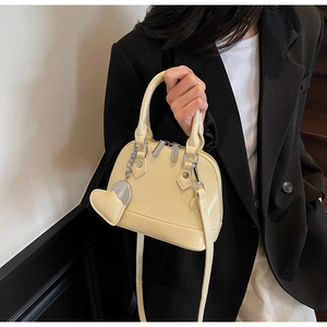 Detail of cream yellow shell bag with heart charm and silver chain strap