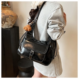 Detail of black glossy tote bag featuring white stitching and cute brown plush bear charm