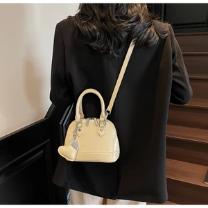Detail of a creamy yellow shell bag with smooth leather finish and a heart charm