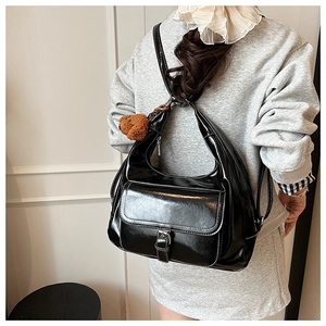Rear view of a black glossy tote bag with a small brown plush bear charm detail