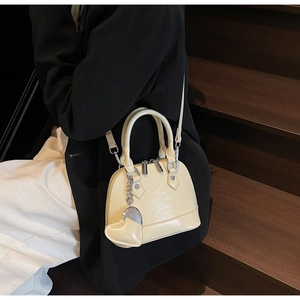 Detail view of cream shell handbag featuring glossy leather texture and heart pendant