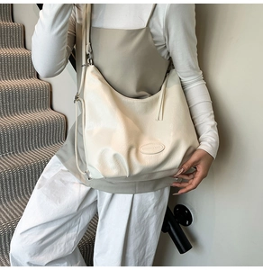 Détail du sac cabas en cuir plissé beige avec écusson logo ovale porté par un mannequin