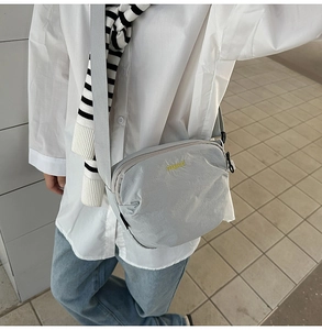 Macro shot of a light grey nylon crossbody bag featuring a yellow manyuashi logo