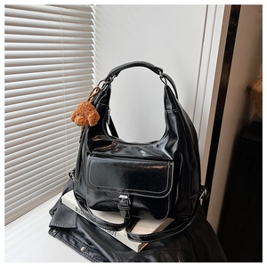 Detail of glossy black hobo tote with front pocket and cute brown teddy bear charm