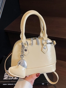 Chic cream shell handbag with heart charm and adjustable strap on a minimalist setup
