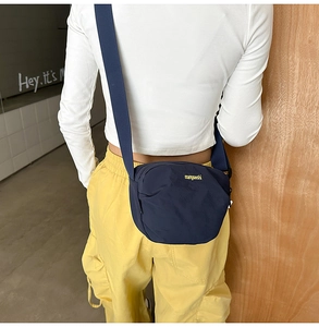 Detail of dark blue nylon crossbody bag with yellow text on model for casual styling