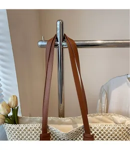 Détail d'un sac cabas tissé beige avec des bandoulières en cuir marron foncé sur cintre