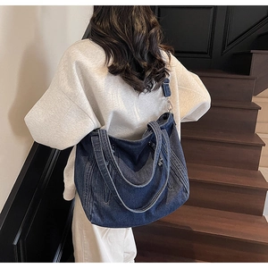Grand sac cabas en jean bleu foncé porté par un mannequin dans un escalier moderne