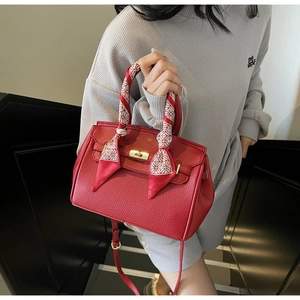 Detail of red lychee leather handbag with gold twist lock and decorative scarf on handle