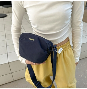 Detail of navy blue nylon crossbody bag with yellow embroidered logo and adjustable strap