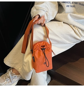 Detail of a bright orange nylon drawstring crossbody bag worn over beige casual wear