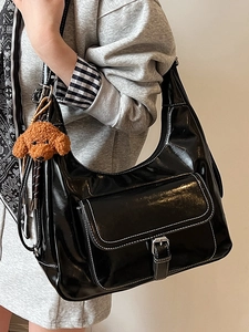 Minimalist black patent leather crescent tote bag with contrast stitching and a plush charm