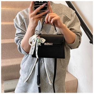 Détail du sac Kelly en cuir grainé noir avec breloque perle et accessoire poupée