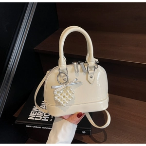 Dettaglio di una borsa a conchiglia bianco crema con ciondolo a cuore e fiocco argento