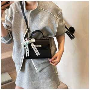 Détail du sac en cuir litchi noir avec nœud en dentelle blanche et fermoir rotatif argenté