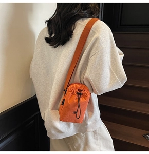 Orange nylon drawstring mini crossbody bag shown on a model for scale and style