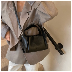 Detail of black lychee grain leather handbag with round handles and adjustable strap
