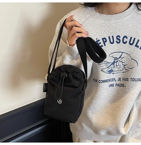 Close-up of black nylon drawstring crossbody bag with woven strap worn by a model