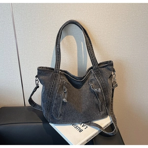 Détail du sac fourre-tout en denim noir délavé avec fermetures éclair à pompons et bandoulière