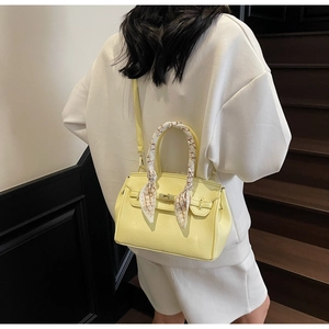 Pale yellow lychee leather bag with scarf-wrapped handle worn by a model in casual style