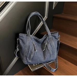 Détail du sac cabas en jean bleu foncé avec surpiqûres blanches et boucles sur un escalier