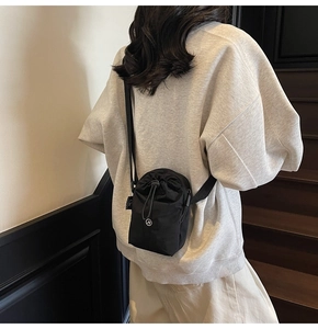 Detail of minimalist black nylon drawstring crossbody bag with circular logo on a model