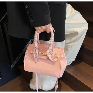 Detailed close-up of pink litchi grain leather handbag with gold lock and silk scarf