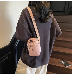Pink drawstring nylon crossbody bag worn on a model against a wooden staircase