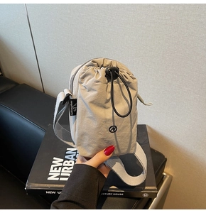 Detail of a grey nylon drawstring crossbody bag with wide strap and branded side label