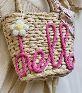 Close-up of handmade straw bag with pink Hello embroidery and floral silk scarf detail