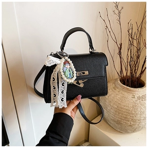 Détail d'un sac noir à motif litchi avec boucle métallique et pendentif en perles