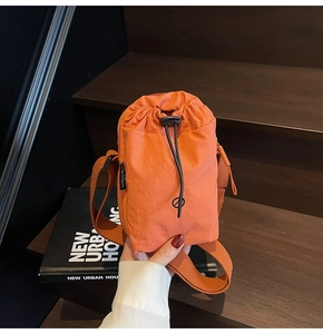 Close-up of orange nylon crossbody bag with drawstring closure on a wooden staircase