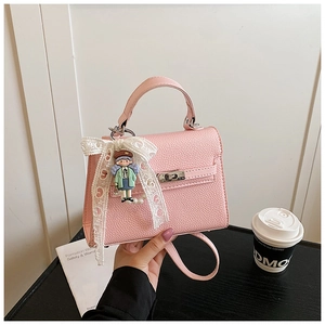 Détail d'un sac à main rose en cuir grainé avec nœud en dentelle et breloque cartoon