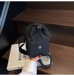 Detail of black nylon drawstring crossbody bag with round N logo and side zipper