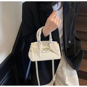 Close-up of a white lychee leather handbag with golden lock and silk scarf on handle