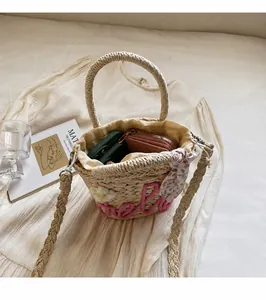 Detail of straw bucket bag with pink hello lettering and white flower on fabric background