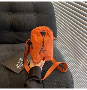 Detail of orange nylon mini crossbody bag with drawstring closure and wide fabric strap